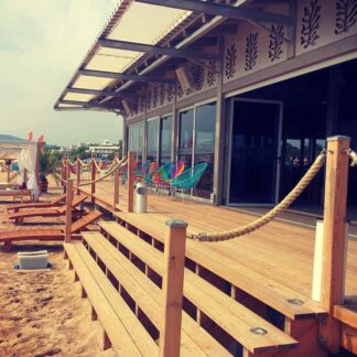 Pasarelă de lemn cu mână curentă din frânghie, în fața unui restaurant de plajă
