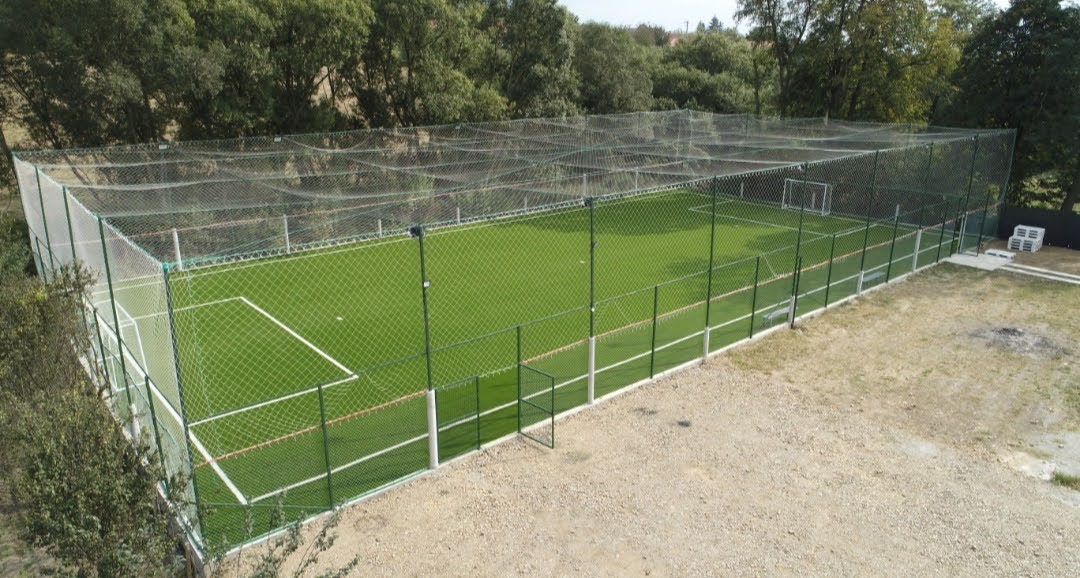 Teren de fotbal cu gazon sintetic, împrejmuit și acoperit complet cu plasă verde de protecție