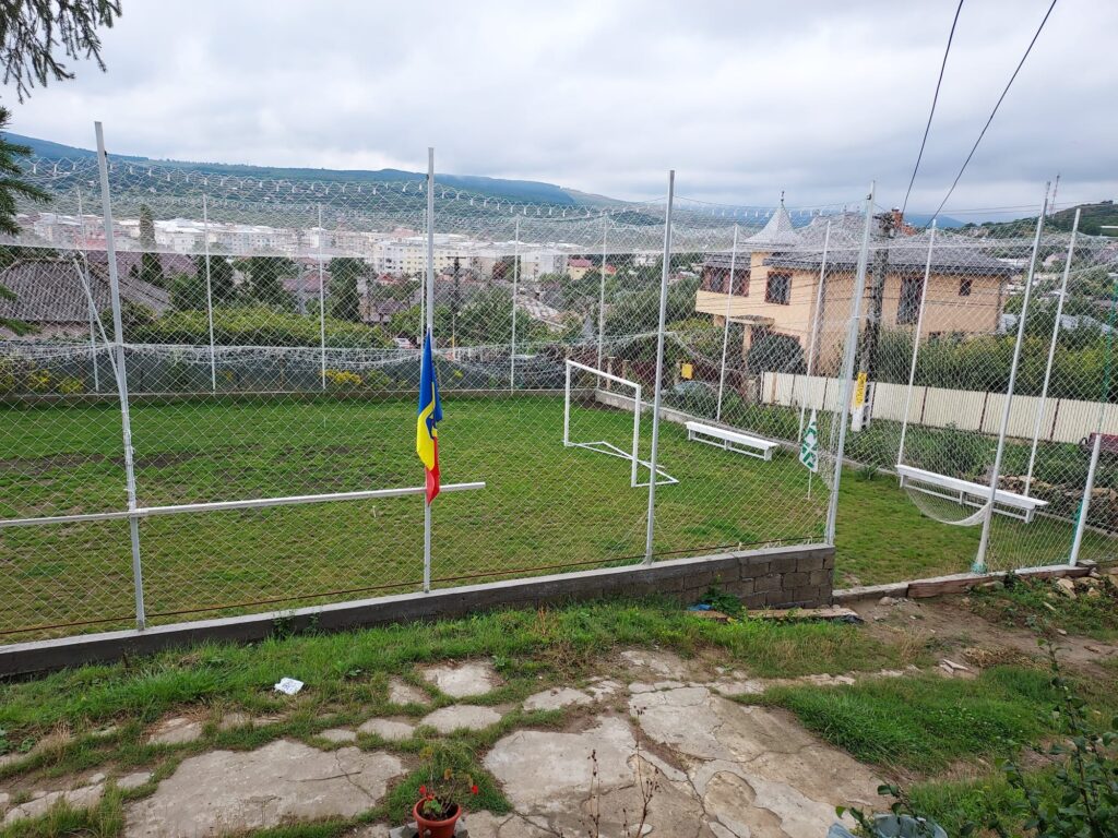 Teren de minifotbal împrejmuit și acoperit cu plasă de protecție, cu priveliște peste oraș