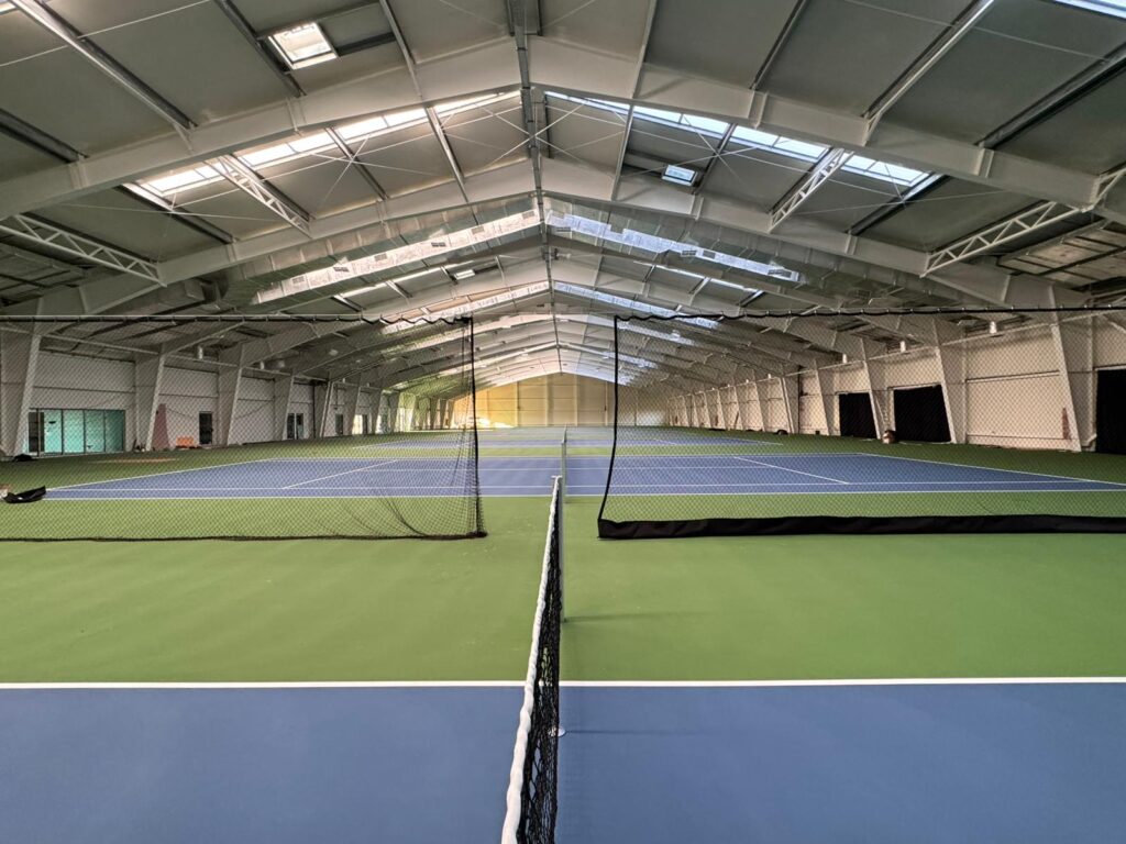 Sală de tenis cu mai multe terenuri, separate prin plase negre montate pe cabluri