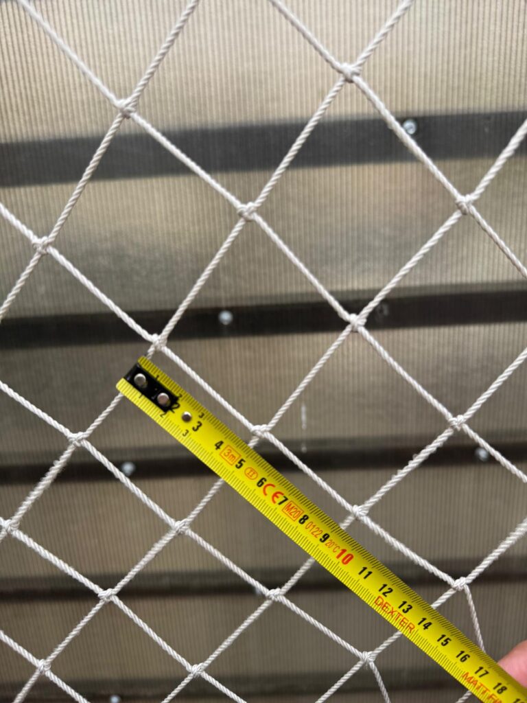 Plasă albă înnodată cu o ruletă galbenă așezată pe ochiuri pentru a arăta mărimea lor