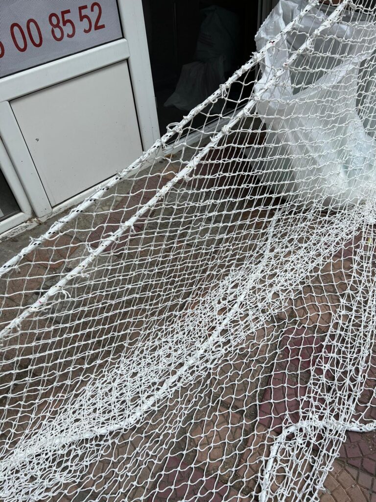 Plasă mare desfășurată pe trotuar, cu frânghia de bordură și flotoare