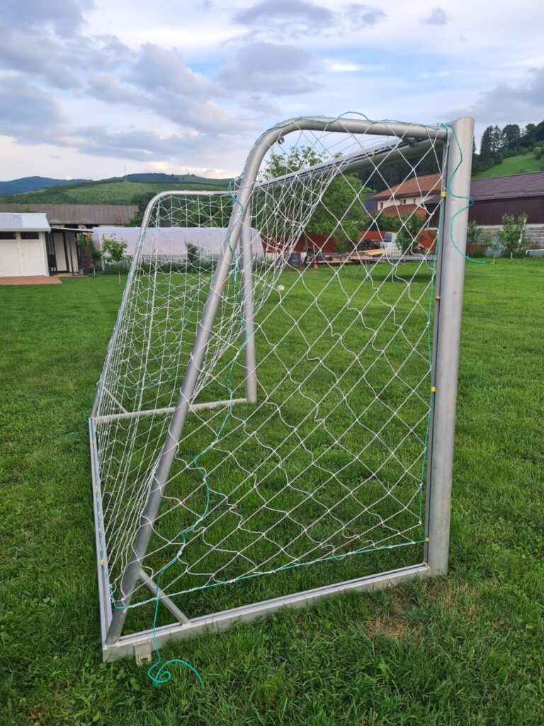 Poartă metalică de fotbal cu plasă albă, pe gazon, cu dealuri în fundal